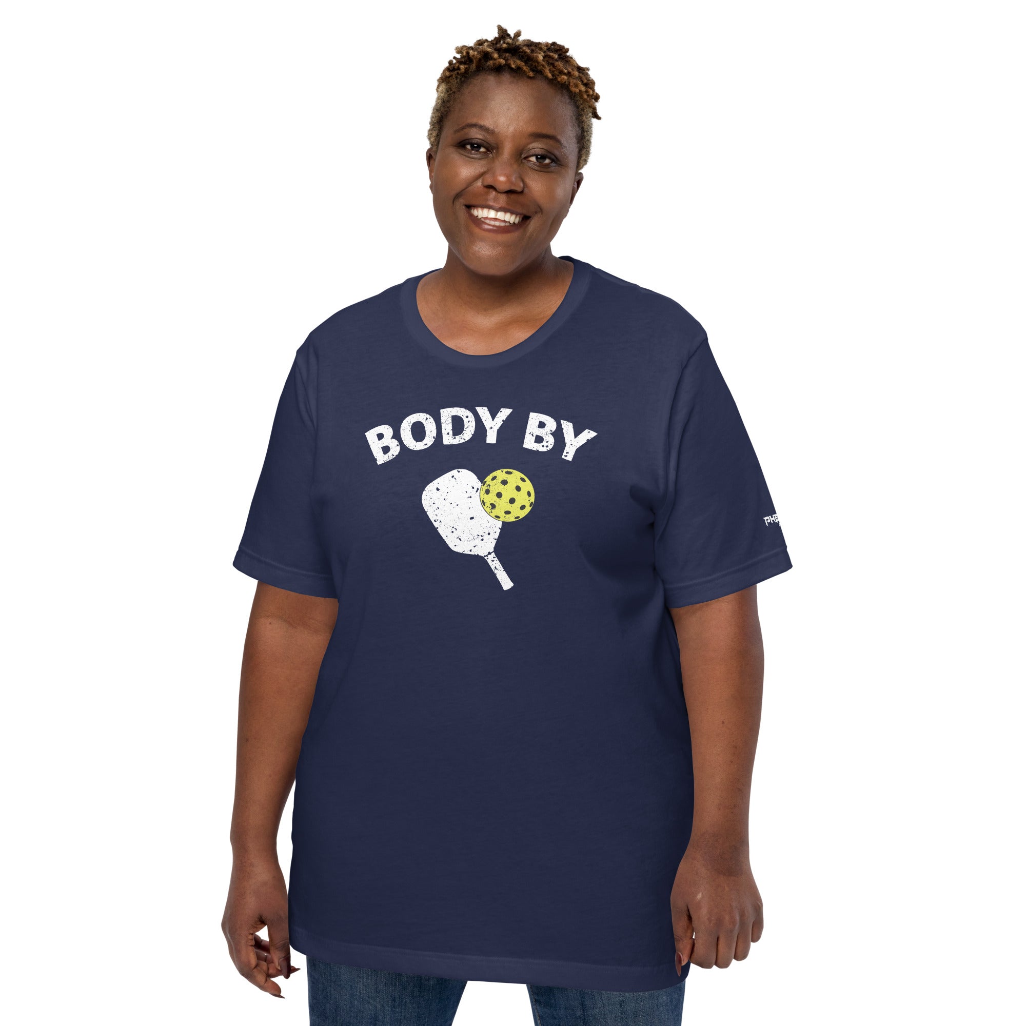 smiling plus sized woman wearing navy blue body by pickleball shirt apparel with paddle and ball weathered look front view