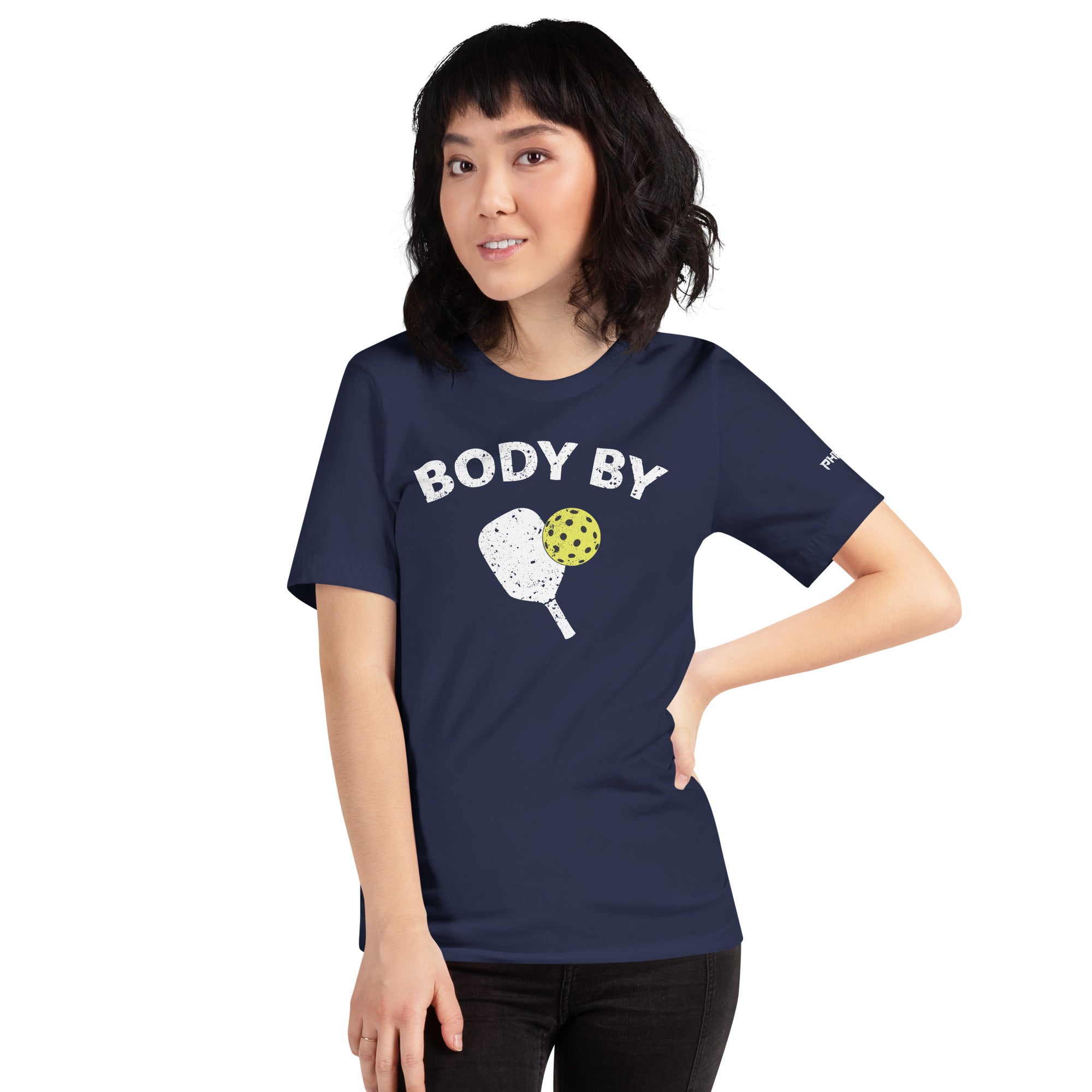 smiling asian woman petite wearing navy blue body by pickleball shirt apparel with paddle and ball weathered look right side view