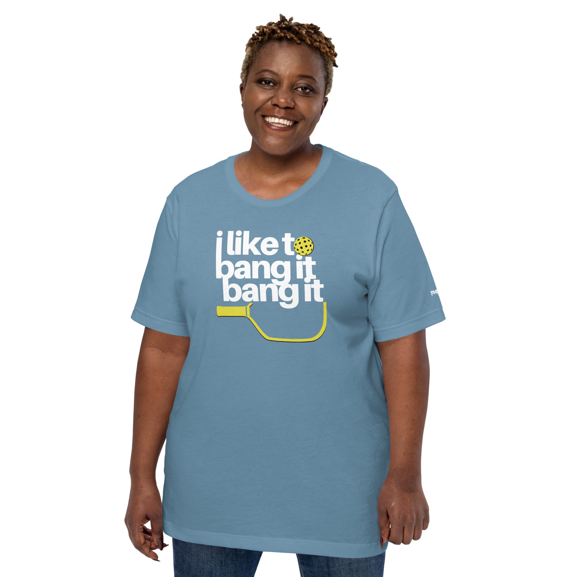 smiling plus sized woman wearing light blue i like to bang it bang it pickleball shirt performance apparel front view